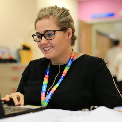 NHS working with rainbow lanyard smiling while using a laptop in a hospital